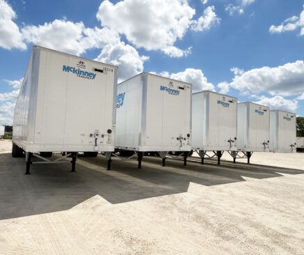 The back of four Mckinney trailers in a parking lot with a blue sky in the background.